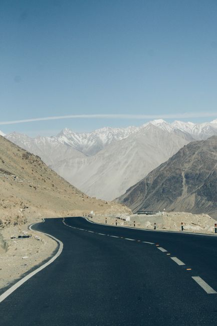 A winding road leads through majestic mountains under a clear blue sky, offering a breathtaking scenic view.