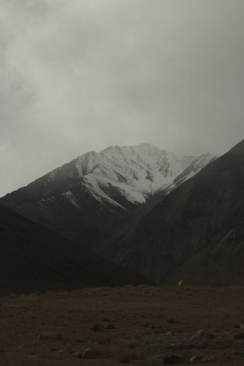 Free A breathtaking view of a snowcapped mountain peak surrounded by cloudy skies and rugged terrain. Stock Photo