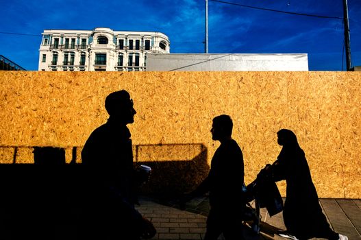 People walking past a building in Istanbul, captured as silhouettes in bright sunlight.