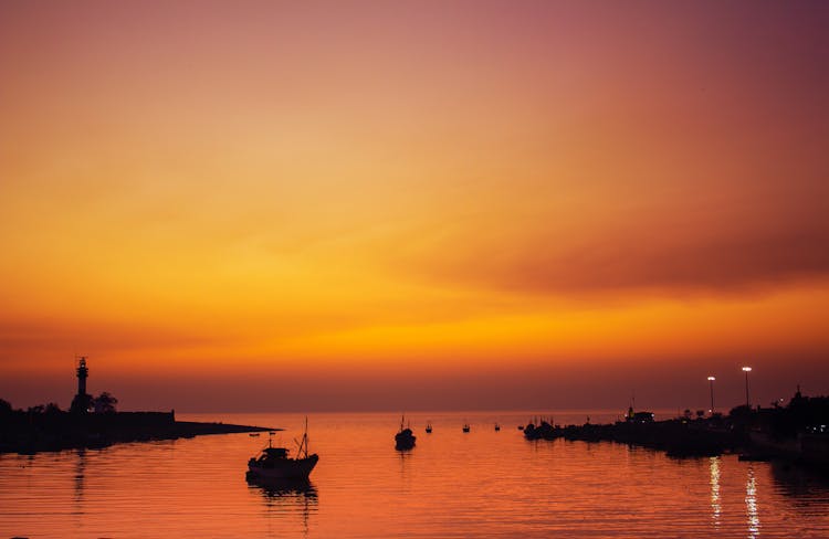 Silhouette Of Boats On Sea Near Port Area During Sunset