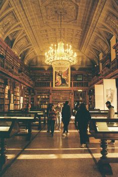 Ornate library interior in Italy featuring a grand chandelier and visitors exploring the space.