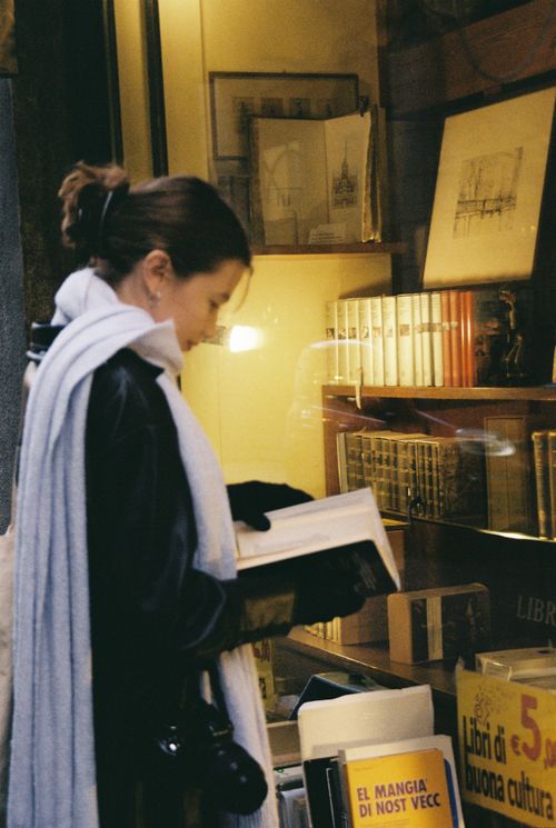 Free A woman reads a book by a window in a Milan bookstore, surrounded by classic volumes and art. Stock Photo