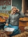 Smiling vendor using cellphone at vegetable market with vibrant produce display.