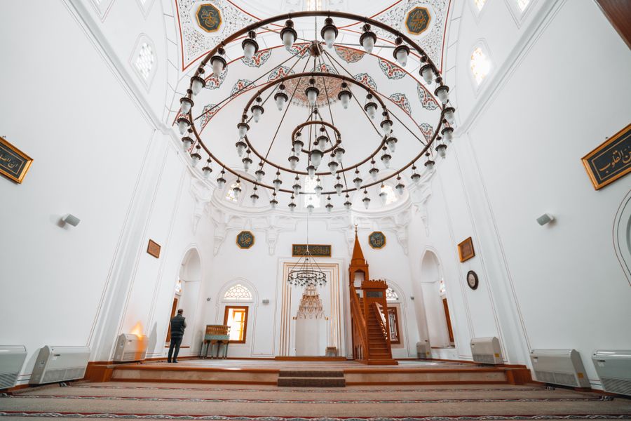 A bright white mosque interior with a chandelier hanging from the dome