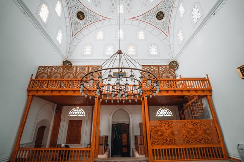 Free A beautifully detailed mosque interior showcasing a wooden balcony, intricate patterns, and a large chandelier. Stock Photo