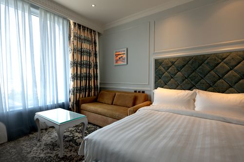 Free Luxurious hotel room featuring a plush bed, sofa, and patterned curtains creating a cozy ambiance. Stock Photo