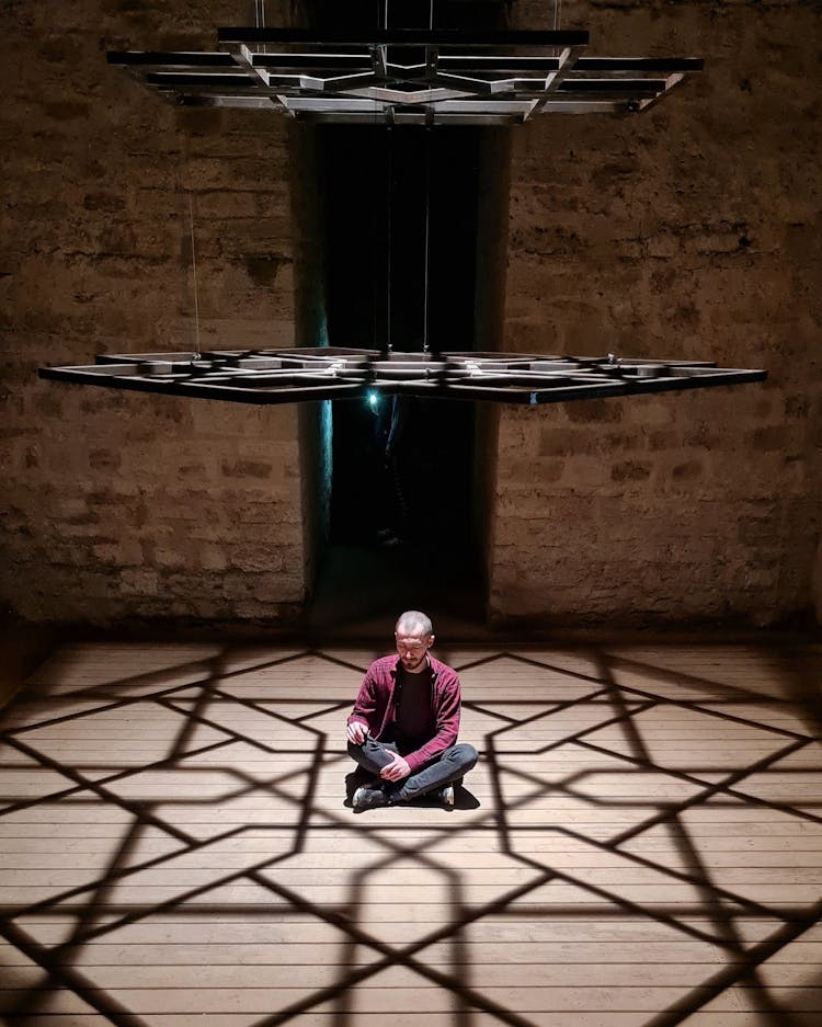 Man Sitting On Sunlit, Wooden Floor In Empty Room