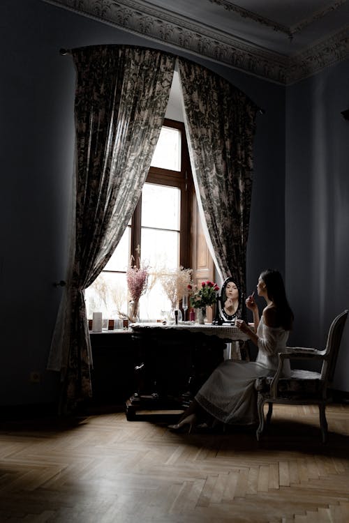 Woman Sitting in Vintage Room and Applying Makeup