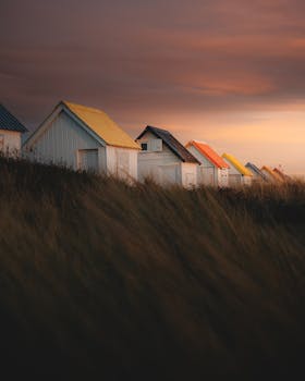 Vibrant beach huts with colorful roofs under a dramatic sunset sky, located in Gouville-sur-Mer, Normandie.