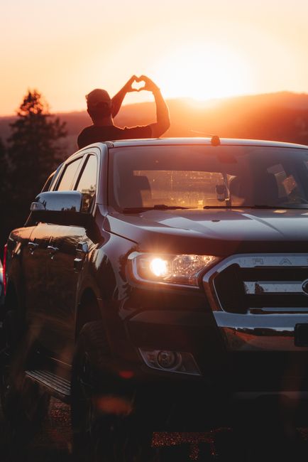 Silhouette of a person making a heart gesture during a sunset road trip with a pickup truck.
