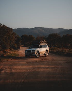 A lone SUV parked on a dirt road amidst a serene mountain landscape at twilight, perfect for adventure themes.