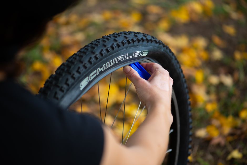 A person repairing a bicycle tire outdoors with fallen autumn leaves in the background.