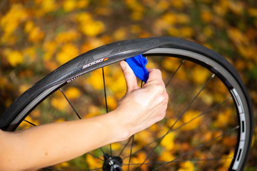 Person repairing a bicycle tire with a tire lever in an autumn setting.
