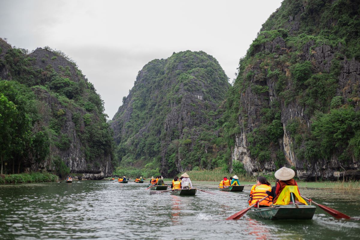 Tourists paddling small rowboats through a lush green river canyon with steep rock walls