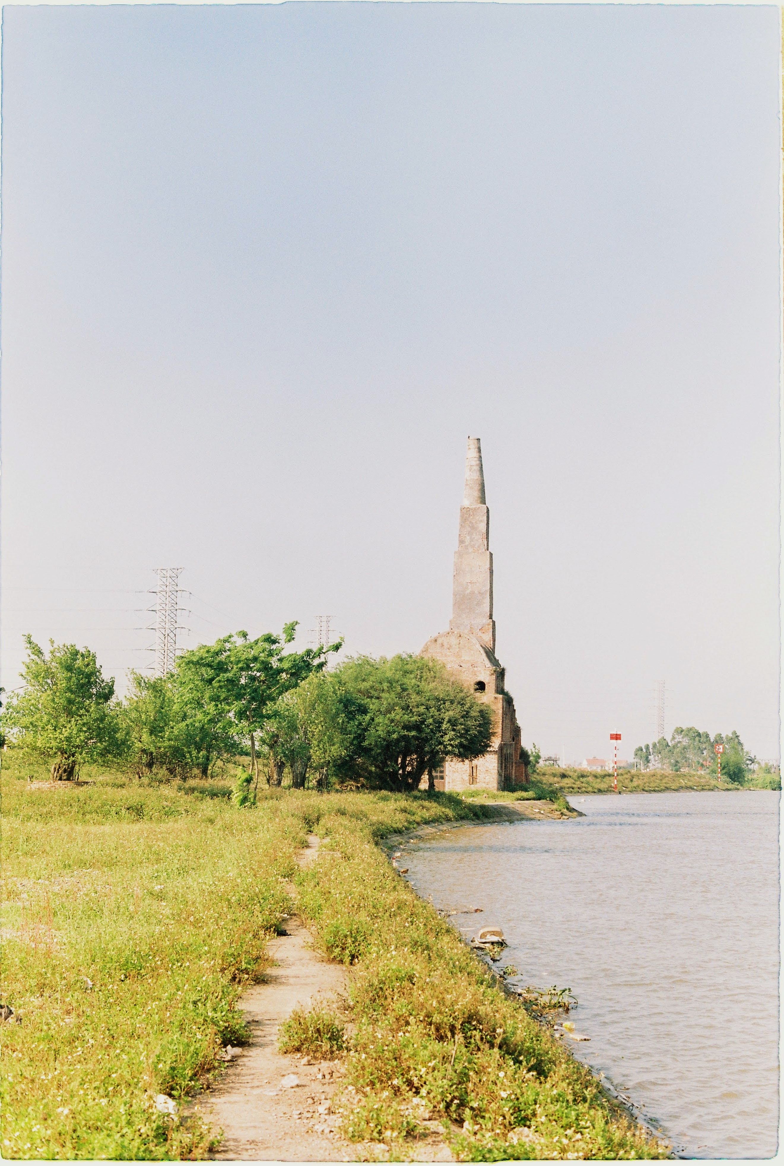 An old tower ruins stands beside a serene riverside under a clear sky.