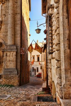 Explore the historic charm of a Montepulciano alley with rustic architecture and vibrant flags.