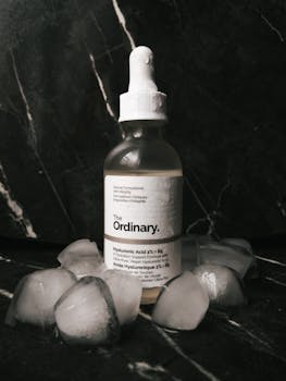 Close-up of hyaluronic acid skincare product with ice cubes on marble.