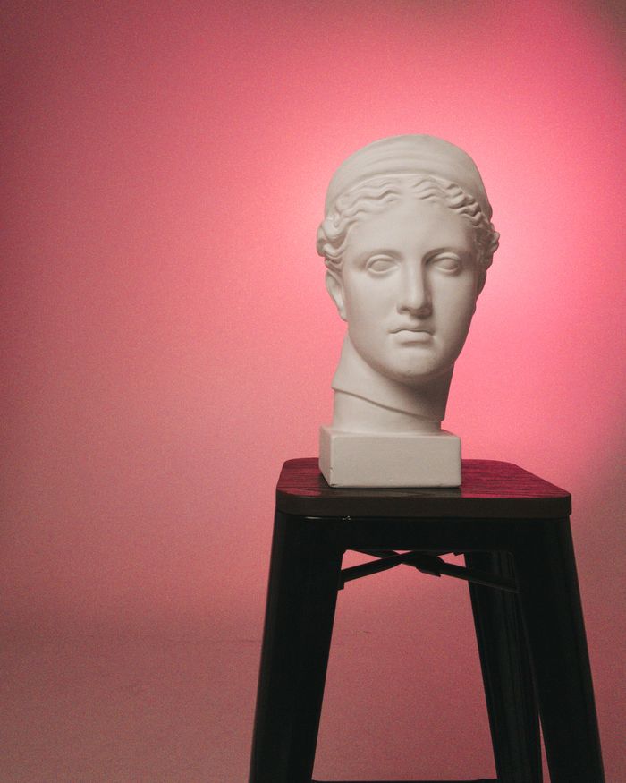Plaster cast of a classical head on a stool under pink light. Photo by Iryna Varanovich on Pexels.