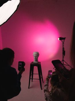 Photograph of a sculpture in a studio setting with people capturing it using smartphones.