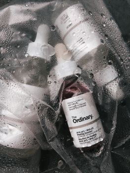 Artistic shot of The Ordinary skincare bottles in a textured plastic bag with water droplets.