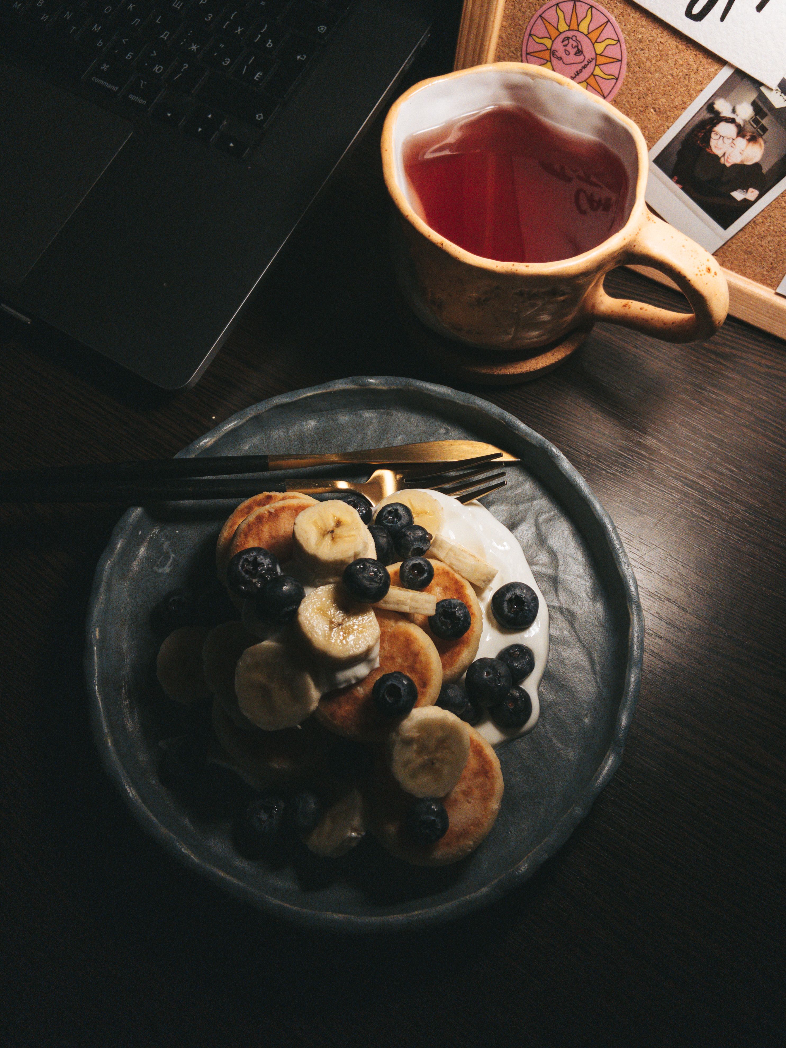 Cozy evening setting with pancakes topped with fruit and a warm cup of tea.