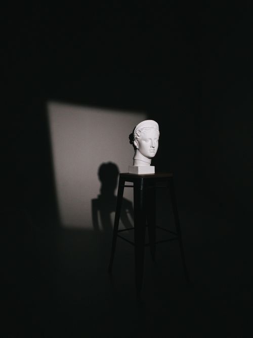 Free Artistic still life of a bust on a stool in a studio, illuminated dramatically. Stock Photo