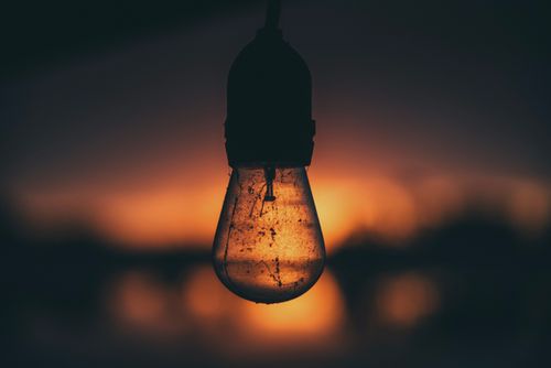 Free A silhouette of a hanging light bulb against a vibrant sunset backdrop, capturing a dramatic and moody atmosphere. Stock Photo