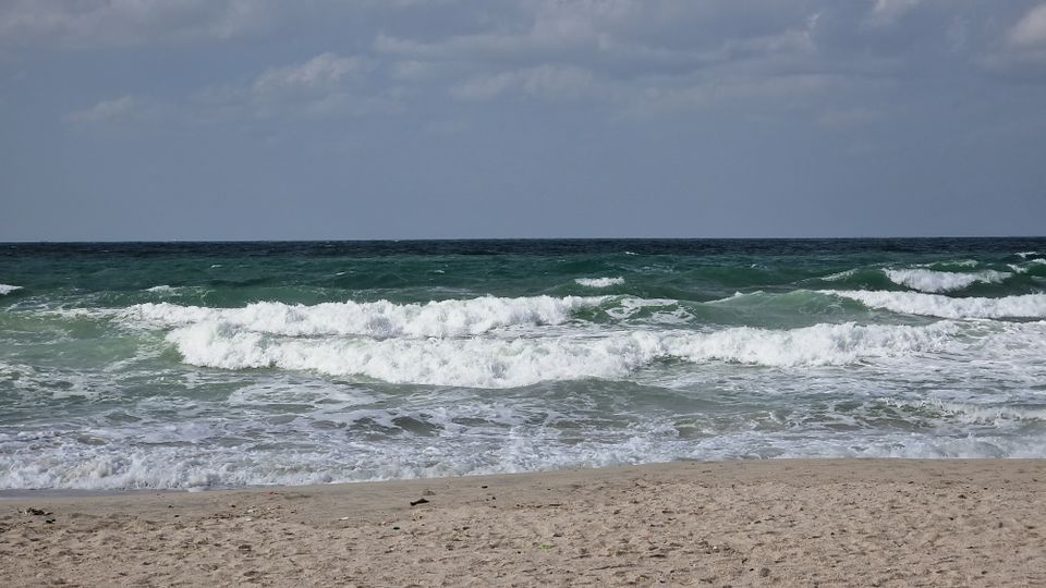 Fesselnder Blick auf Meereswellen, die an einem bewölkten Tag an einem Sandstrand brechen.