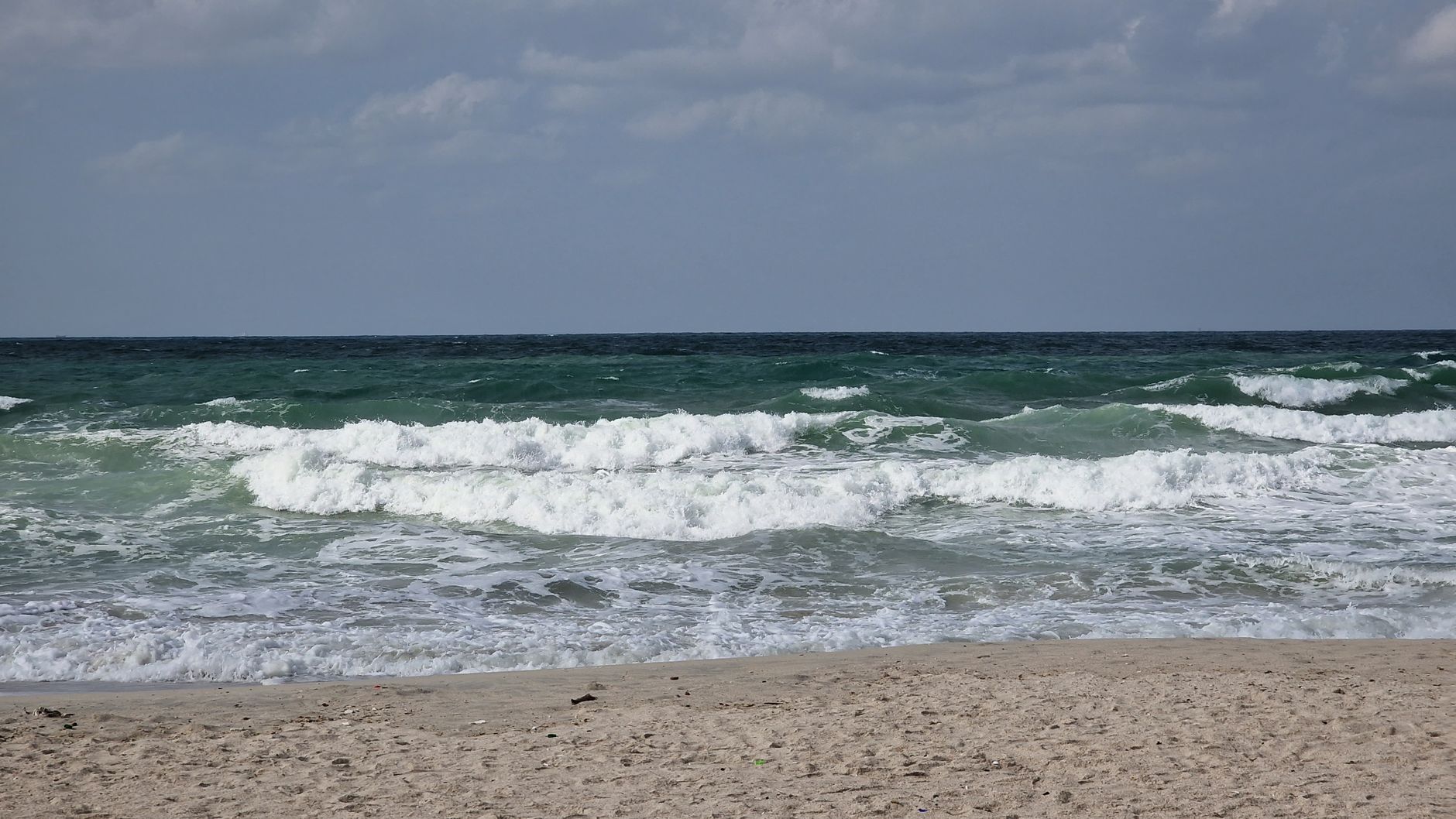 Atractiva vista de olas del océano rompiendo en una playa de arena bajo un cielo nublado.
