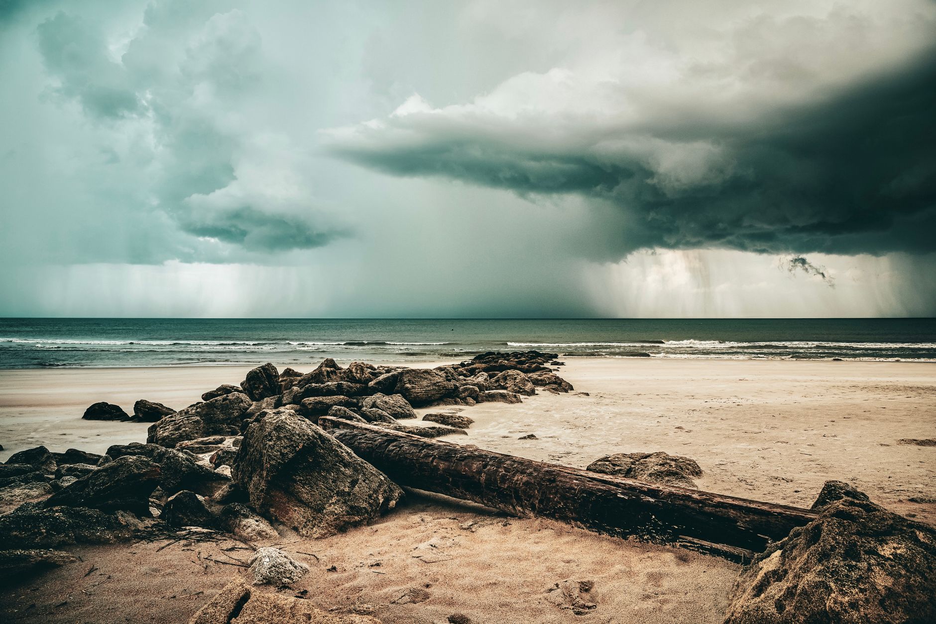 Una escena dramática de una tormenta que se acerca a una playa de arena con rocas bajo un cielo nublado.