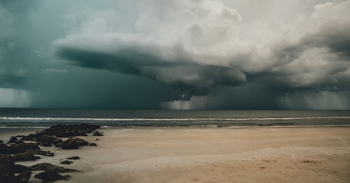 Photo by Connor Scott McManus Majestic storm clouds gather over a tranquil sandy beach, showcasing nature's power.