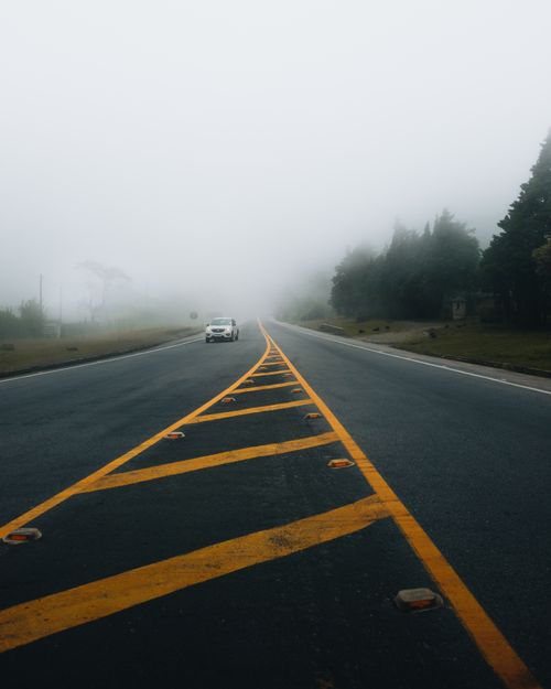 Free A misty rural road leading into fog with a car in the distance, offering a tranquil travel scene. Stock Photo