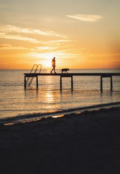 Peaceful sunset scene of person walking dog on Trelleborg pier in Skåne, Sweden.