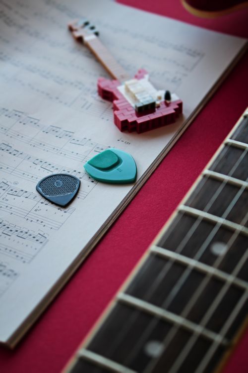 Free Assorted guitar picks on sheet music with a red backdrop and a guitar neck. Stock Photo