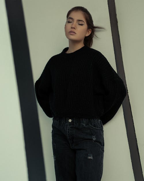 A Woman in Black Sweater Leaning on the Wall with Her Eyes Closed