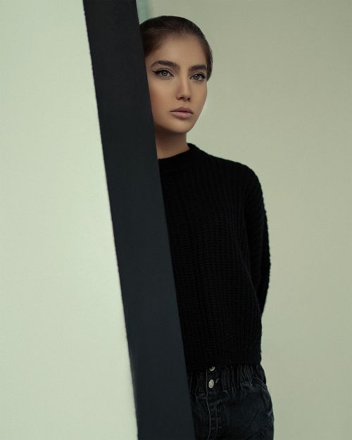 Free Portrait of a fashionable woman in a black sweater posing indoors against a minimalist backdrop. Stock Photo