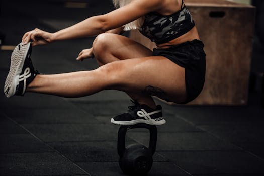 An athletic woman performing balance exercise on kettlebell in a gym.