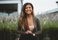 一名女子笑容灿烂地坐在绿树成荫的户外，非常适合生活方式和时尚主题