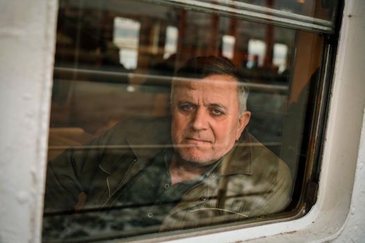 Portrait of a mature man in a brown jacket looking out through a train window.