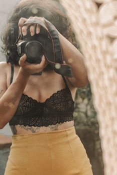 A woman taking a mirror selfie with a DSLR camera wearing a black lace top.