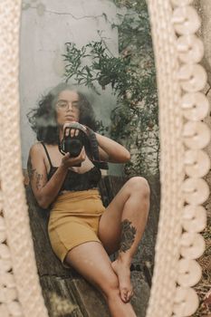 Reflection portrait of a tattooed woman sitting and holding a camera.