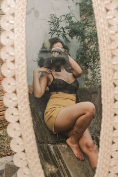 A woman captures a creative mirror selfie while posing outdoors.