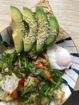 Top view of avocado toast with salad and poached egg for a healthy meal.