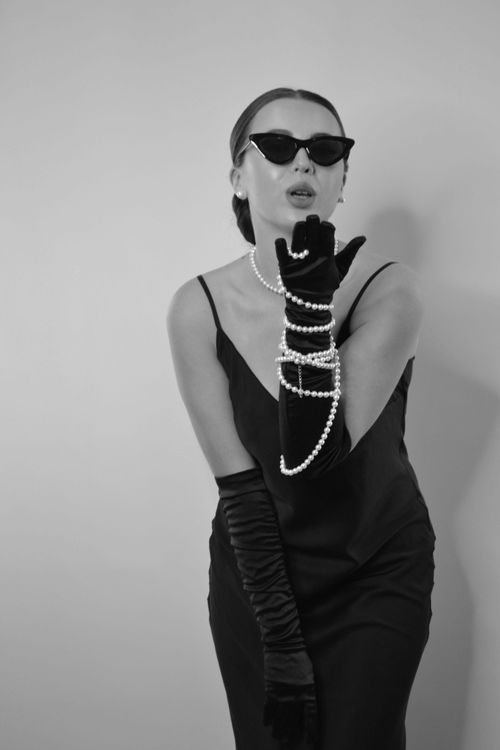 Free Stylish portrait of a woman in a black dress with gloves and pearls, exuding elegance. Stock Photo