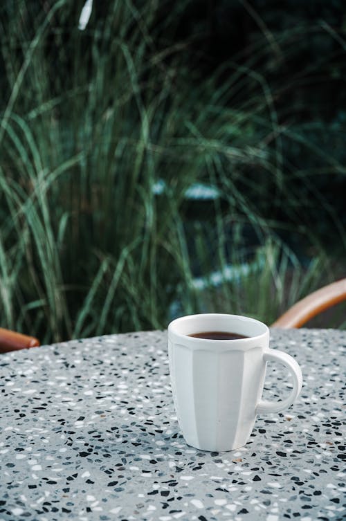 A Mug of Hot Coffee on a Marble Surface Near Green Grasses