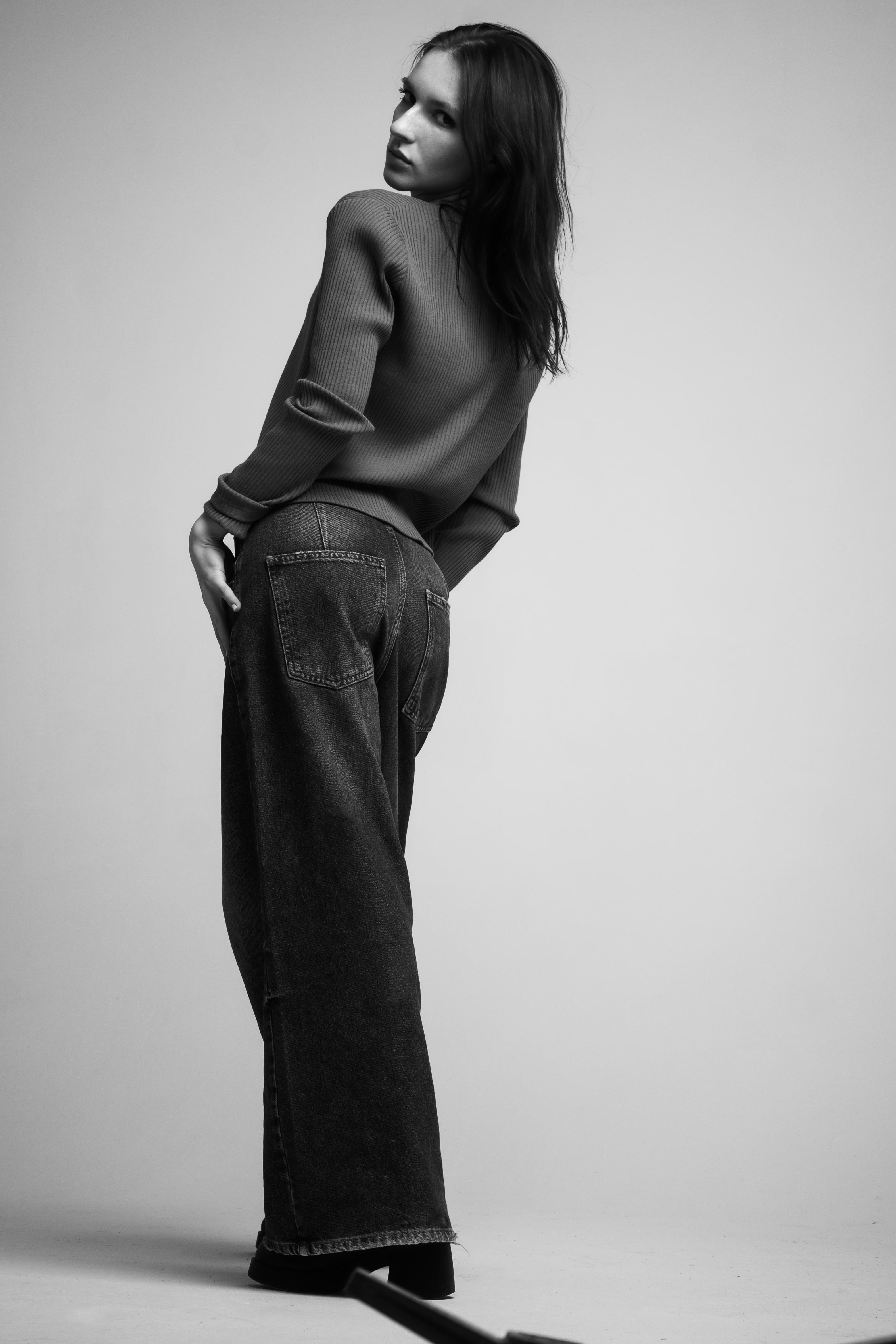 Elegant woman in denim and sweater fashion posing in a monochrome setting.