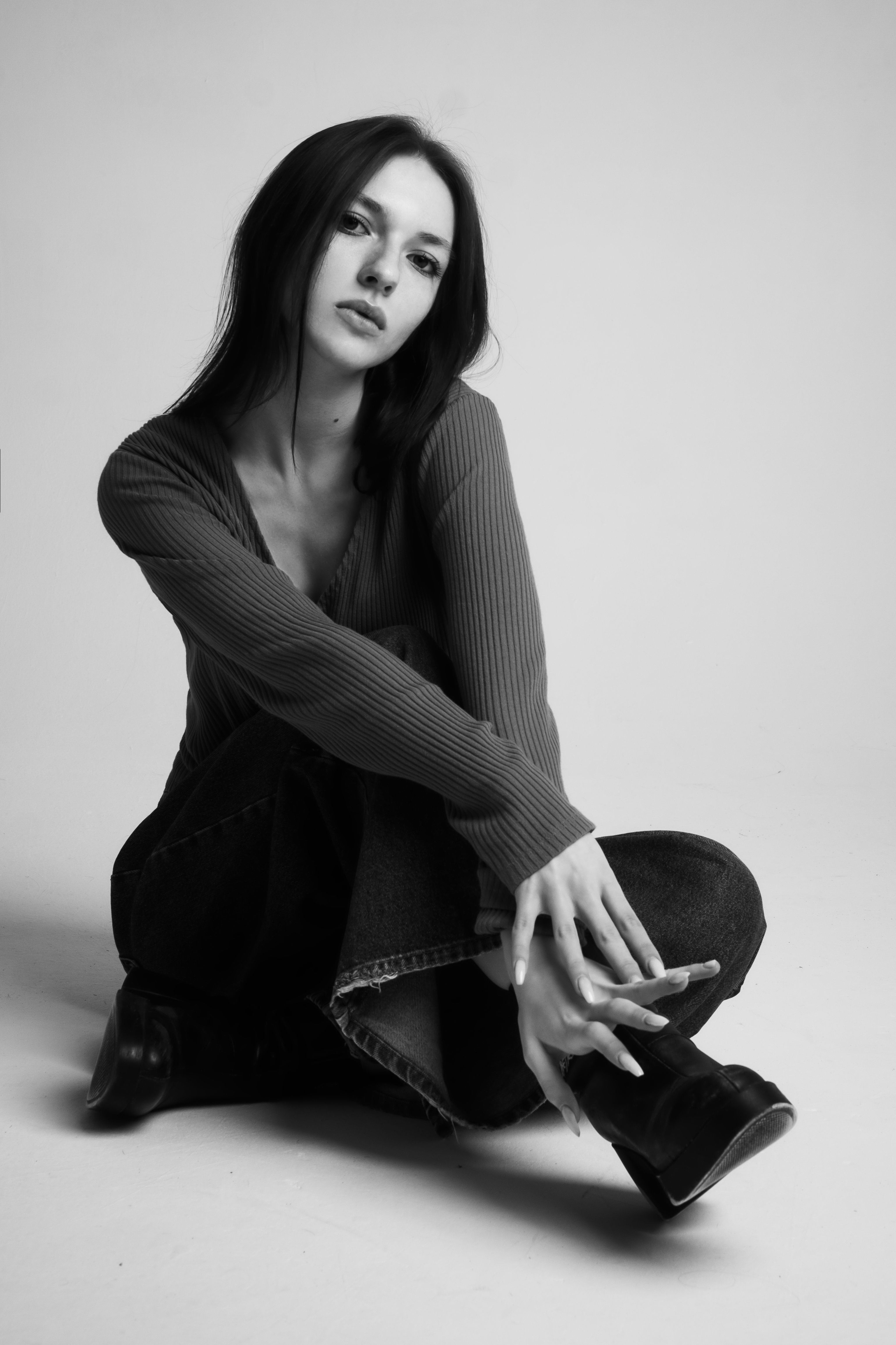Elegant grayscale portrait of a stylish woman sitting indoors in a studio setting.
