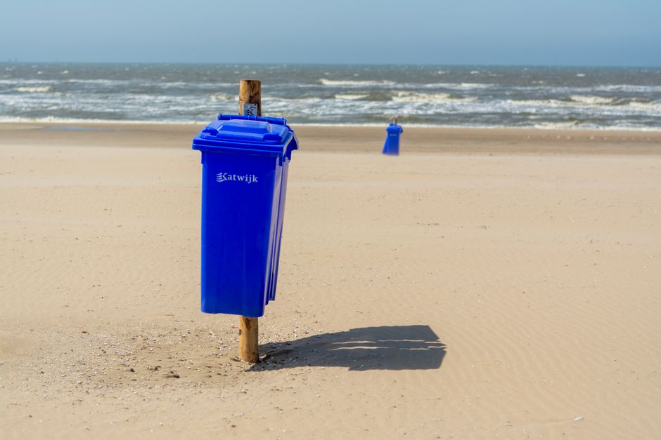 Sunlit beach with blue garbage bins by the sea in Katwijk aan Zee, Netherlands.