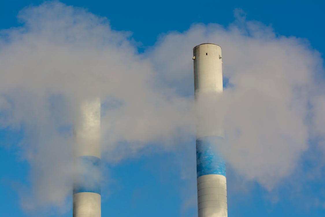 Photo of Two Smoking Industrial Chimneys Against a Blue Sky