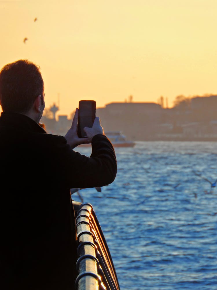 Photo Of A Man Taking Pictures With A Smartphone While Standing On A Boat